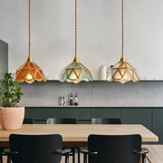 Three decorbites glass vintage pendant lights with amber and teal stained-glass shades hanging by twisted brass cords
