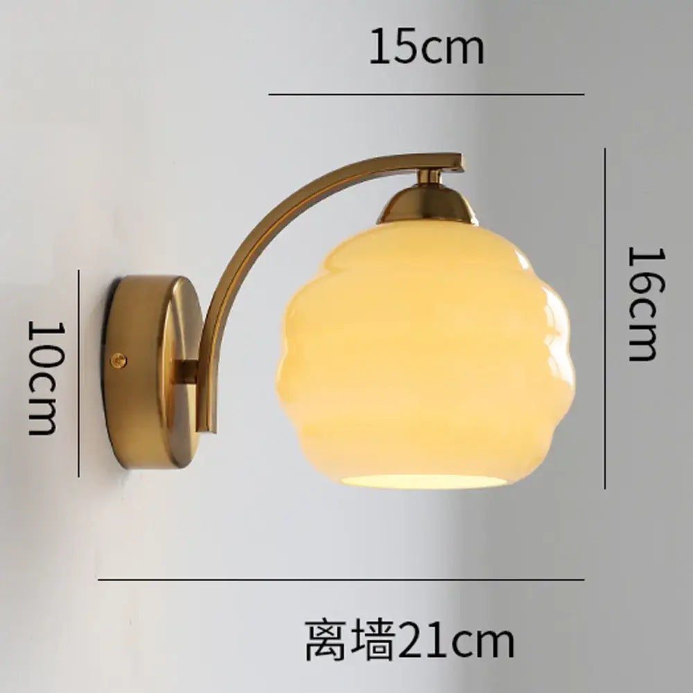 A warm yellow glass wall lamp with a curved brass arm from decorbites glass wall lamp collection for modern interiors