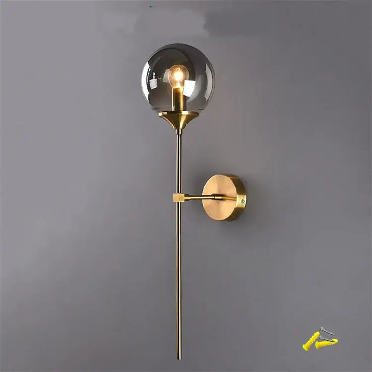 A sleek brass DecorBites glass wall lamp with smoked glass globe and exposed filament bulb for bedroom lighting