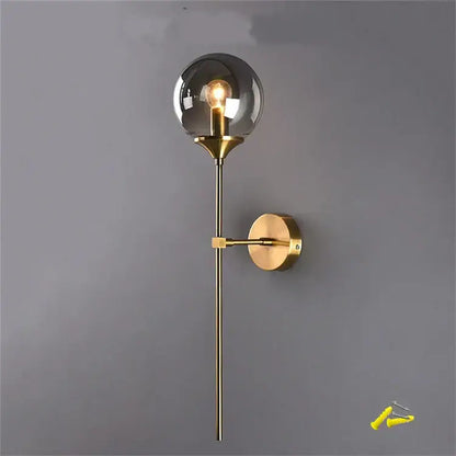 A sleek brass DecorBites glass wall lamp with smoked glass globe and exposed filament bulb for bedroom lighting