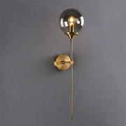 A sleek brass decorbites glass wall lamp with smoked glass globe and exposed filament bulb for bedroom lighting
