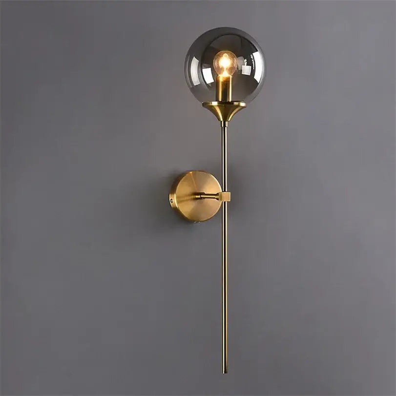 A sleek brass decorbites glass wall lamp with smoked glass globe and exposed filament bulb for bedroom lighting