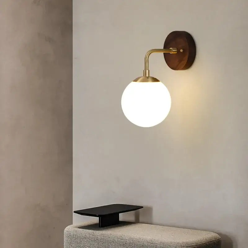 Gold-finished decorbites glass wall light fixture with frosted glass globe and walnut wood backplate with pull chain switch