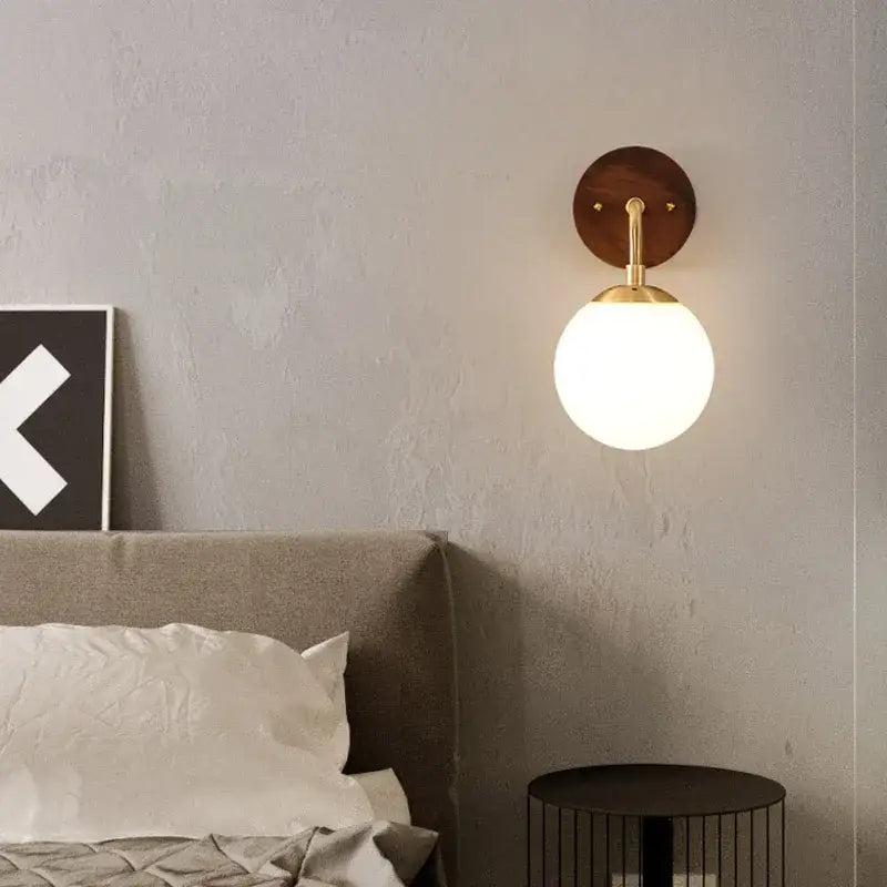 A decorbites glass wall light fixture with a warm spherical glass globe, brass arm, and walnut wood circular backplate