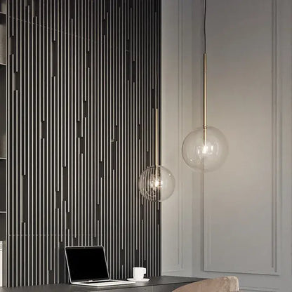 Two modern pendant lights with gold glass bubble shades and brass rods hang from the ceiling in a dining room setting