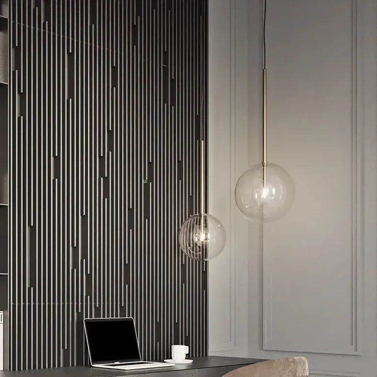 Two modern pendant lights with gold glass bubble shades and brass rods hang from the ceiling in a dining room setting