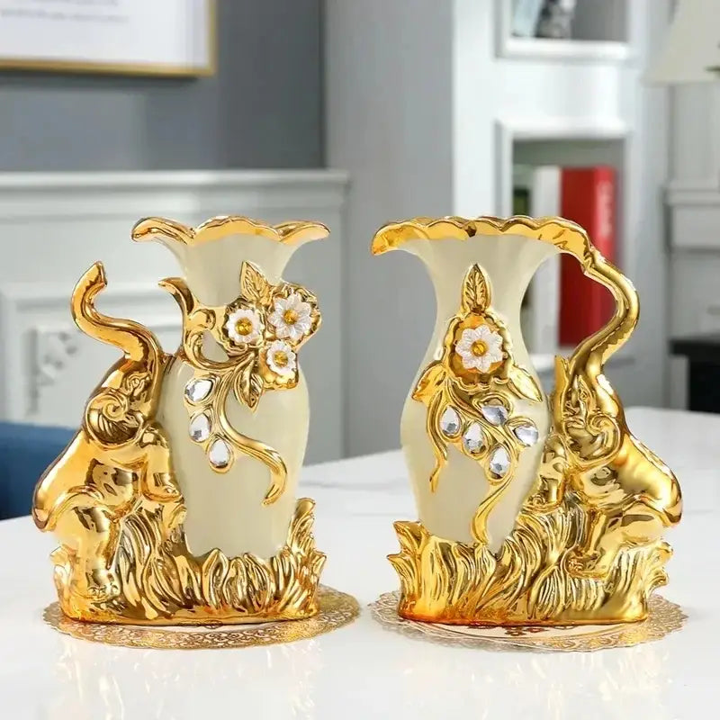 Pair of cream-colored ceramic vases with gold accents and ornate elephant figures featured in a gold glass vase decor by DecorBites™