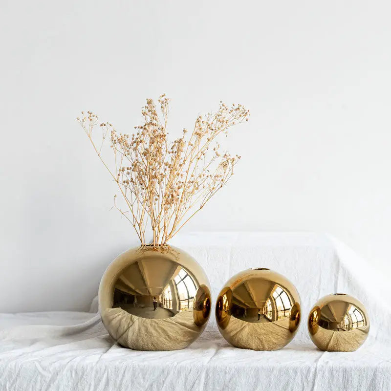 Shiny golden ball ceramic vases in varying sizes arranged in a row on white surface for home decor by decorbites