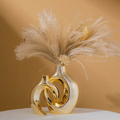 DecorBites™ golden flower vase is a golden ceramic flower vase with an intertwined sculptural design holding dried pampas grass