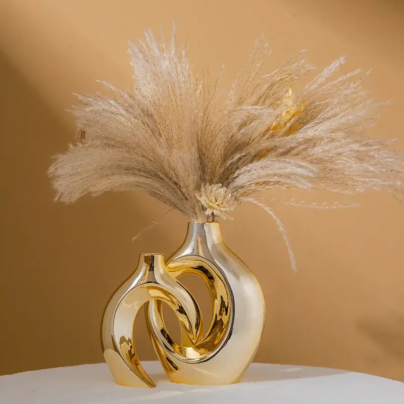 DecorBites™ golden flower vase is a golden ceramic flower vase with an intertwined sculptural design holding dried pampas grass