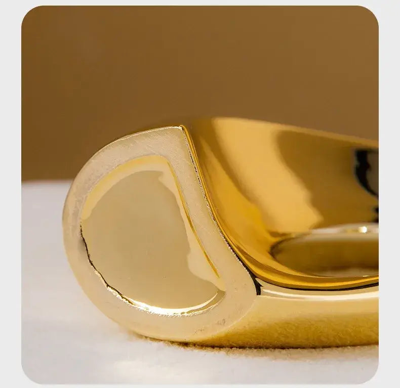 A sleek gold-toned ring with a modern asymmetrical design next to a decorbites golden flower vase for home decor