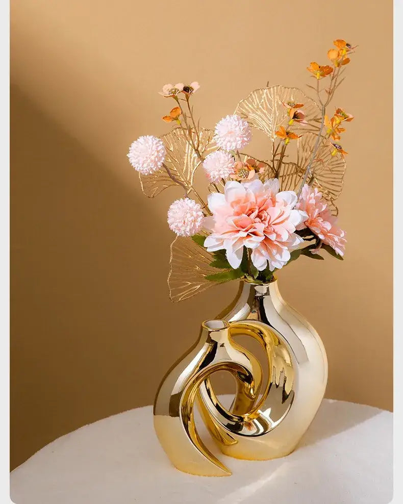 DecorBites™ golden flower vase is a sleek gold-toned ceramic vase with intertwined swirl design holding pink flowers