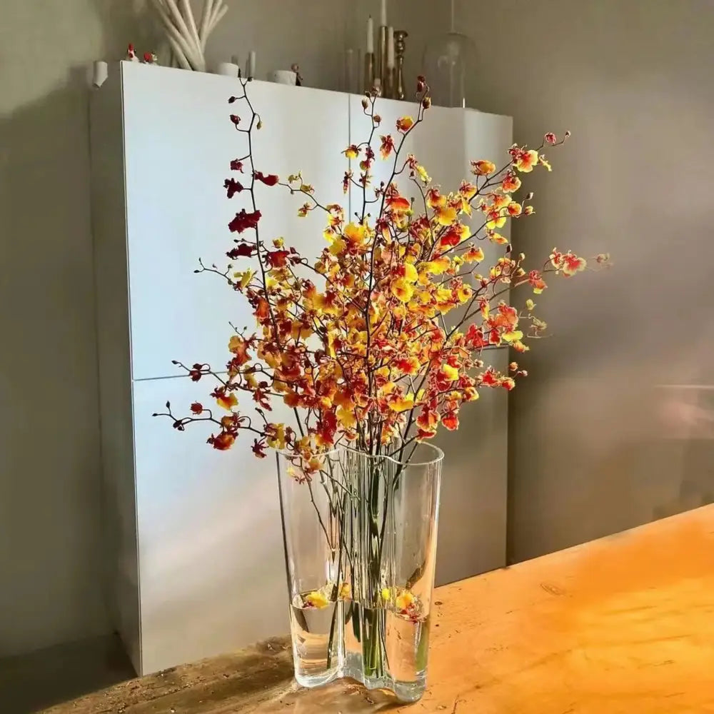 Decorbites™ green glass vase with a tall asymmetrical glass vase holding vibrant yellow and orange orchids for modern decor