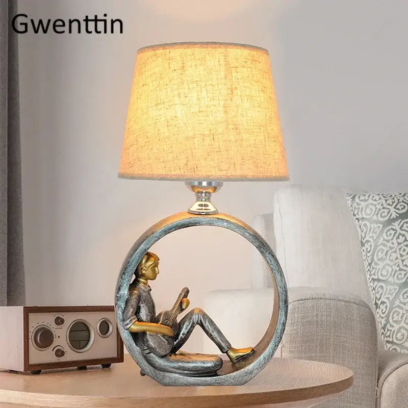 Gwenttin table lamp with brass finish and beige shade featuring sculpted man reading in circular frame, ideal for bedroom reading light