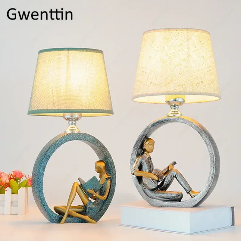Two decorbites guitar girl table lamps with circular bases featuring a reading figure and beige textured shades