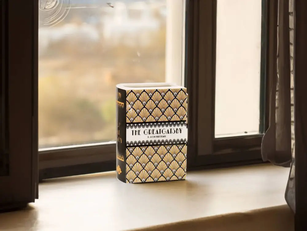 A hardcover edition of the great gatsby beside a decorbites hand-painted white flower ceramic vase for home decor