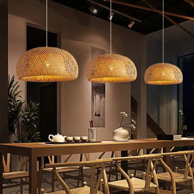 Three warm-toned hand-woven bamboo pendant light chandeliers hang above a wooden dining table by decorbites