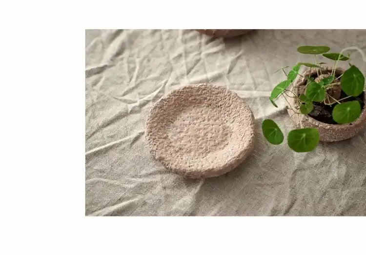 A handcrafted ceramic vase in light beige with a textured surface beside a matching pottery vase holding green plants