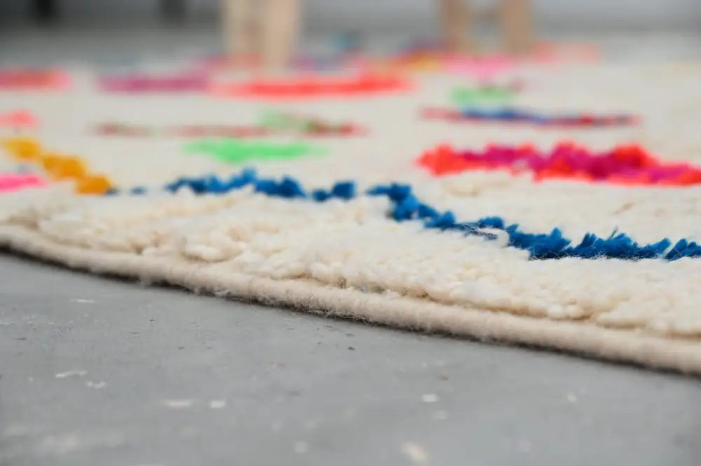 Cream-colored wool moroccan azilal rug with vibrant geometric patterns and fringed edge by decorbites 246 x 146 cm