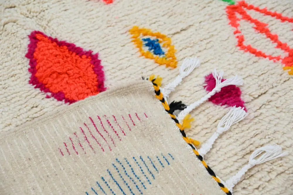 Cream-colored moroccan azilal rug with vibrant hand-knotted geometric patterns and white tassels by decorbites
