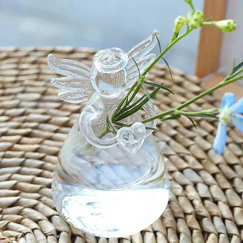 DecorBites™ handmade clear glass angel vase with delicate wings heart detail holding green stems and blue flowers