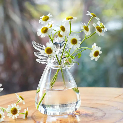 Clear glass handmade angel-shaped vase by DecorBites holding white daisies with yellow centers for home decor