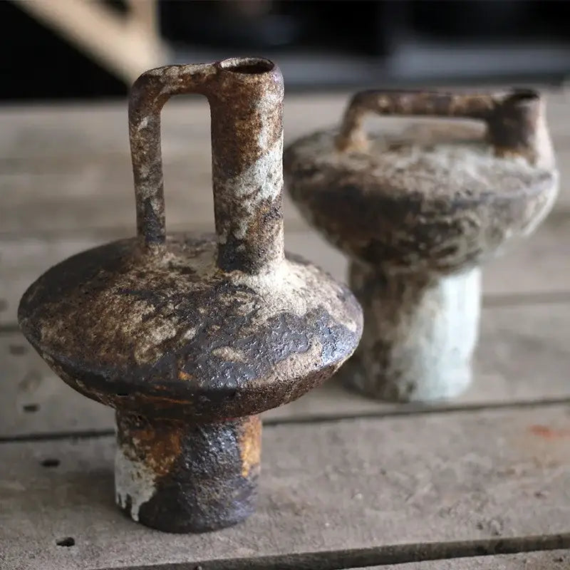 Rusty weathered iron weights with handle and rounded top next to a pottery vase for dried flowers by decorbites