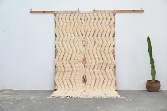 Cream-colored handmade moroccan azilal rug with bold zigzag pattern in muted purples oranges yellows and fringed edges