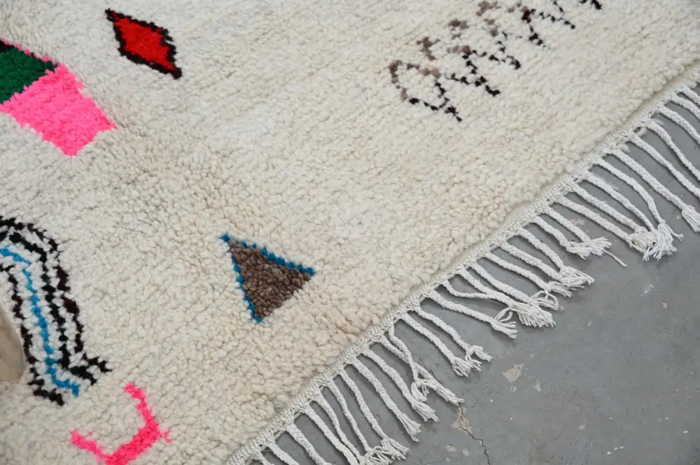 Cream-colored decorbites™ handmade moroccan azilal rug with vibrant geometric patterns in natural wool and white fringe