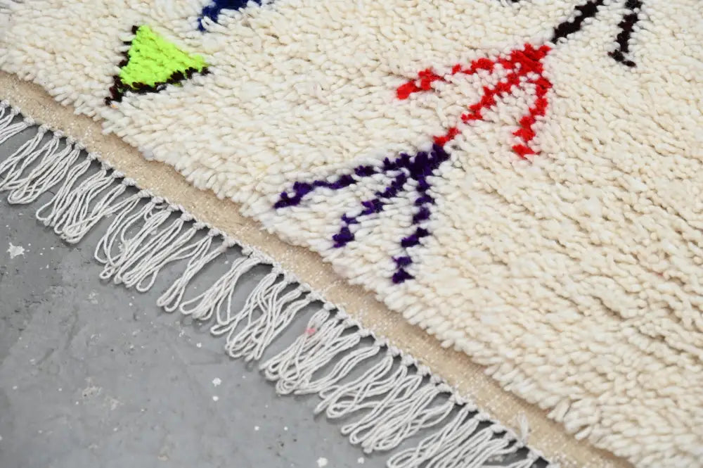 Cream-colored moroccan azilal rug with fluffy texture and vibrant neon green red purple geometric patterns and white fringe
