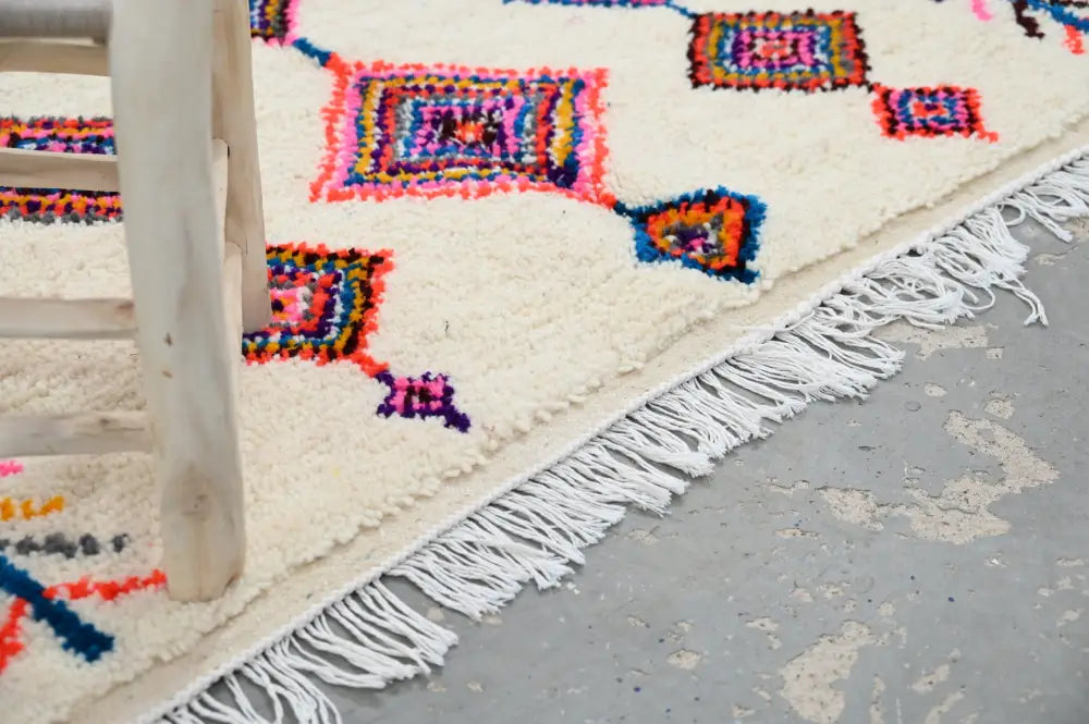 Cream-colored handmade moroccan azilal rug with vibrant geometric patterns and long white fringe 236x155cm decorbites