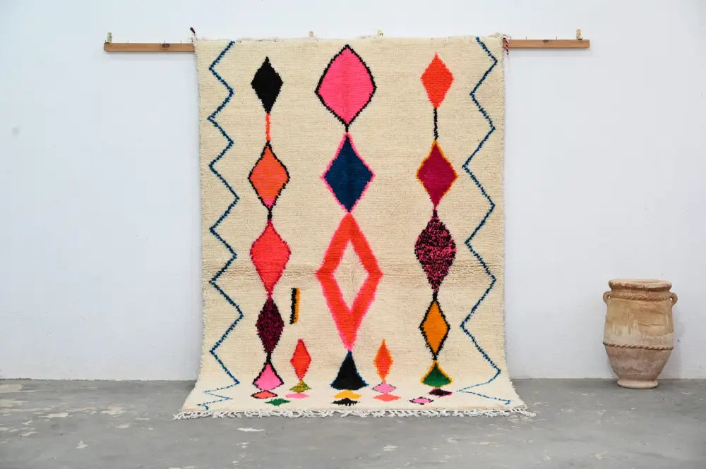 Beige handmade moroccan azilal rug with vibrant colors bold geometric patterns textured woolen surface and fringed edges