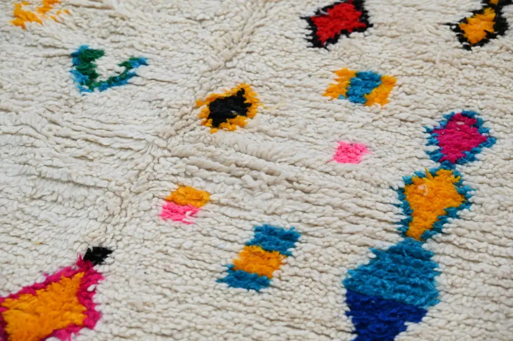 A cream-colored decorbites™ handmade moroccan azilal rug 240x132cm with vibrant geometric patterns in bold hues