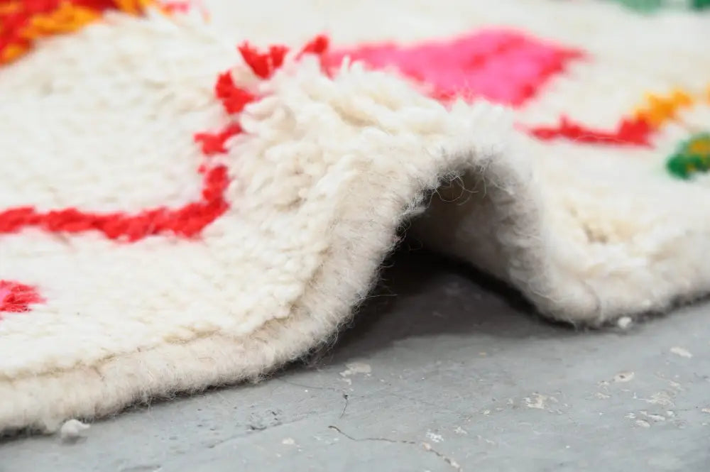A plush white decorbites handmade traditional azilal rug with vibrant red pink and orange geometric patterns