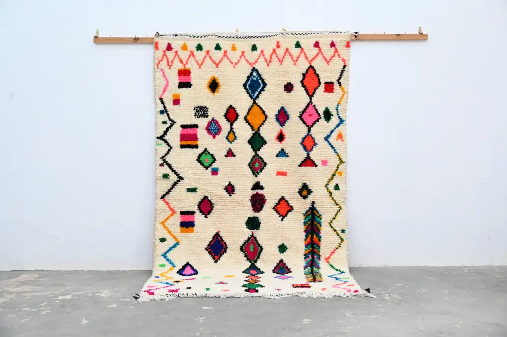 A vibrant cream-colored handmade moroccan azilal rug 240x144cm with bold geometric patterns in multiple colors