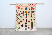 A vibrant cream-colored handmade moroccan azilal rug 240x144cm with bold geometric patterns in multiple colors