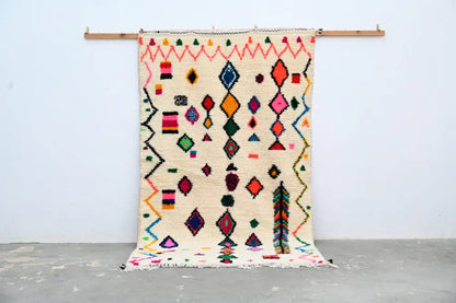 A vibrant cream-colored handmade moroccan azilal rug 240x144cm with bold geometric patterns in multiple colors