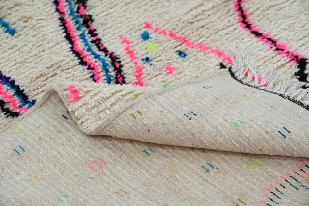 Cream-colored handmade traditional azilal rug with vibrant pink blue and black geometric patterns in textured wool