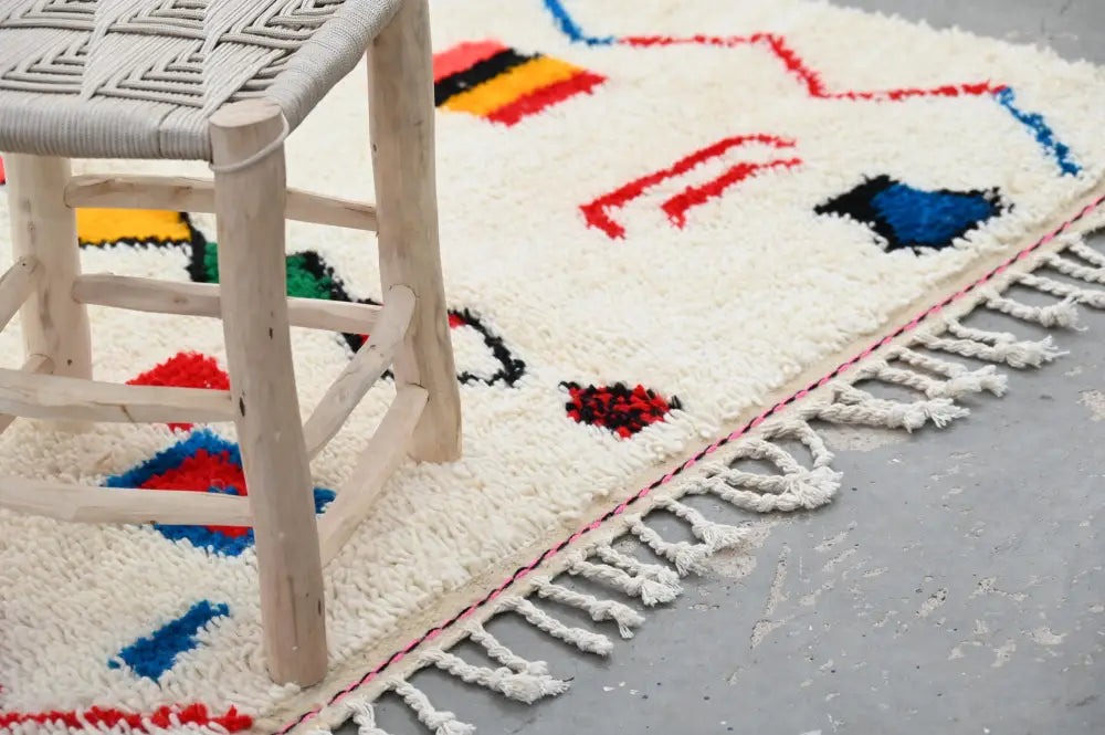 Cream-colored handmade traditional azilal rug with bold red blue yellow and black geometric patterns and fringed edge