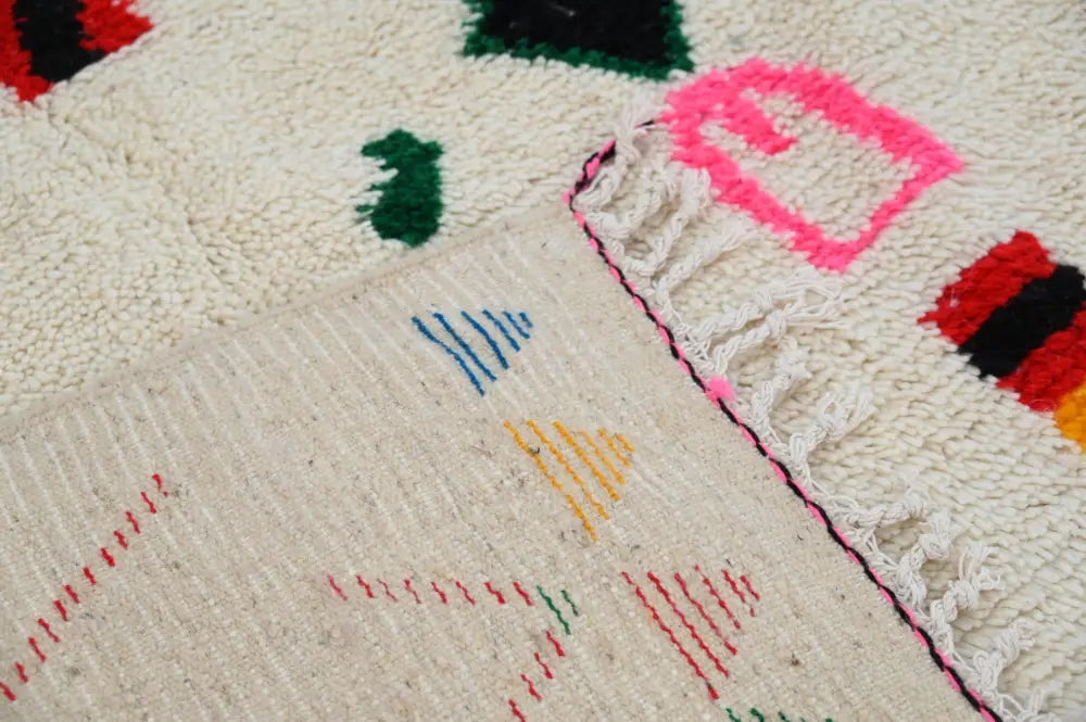 Cream-colored handmade traditional azilal rug with vibrant geometric patterns and fringed edge by decorbites