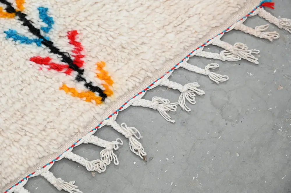 Cream-colored handmade moroccan azilal rug with vibrant red blue orange geometric patterns and white fringe 242x150cm