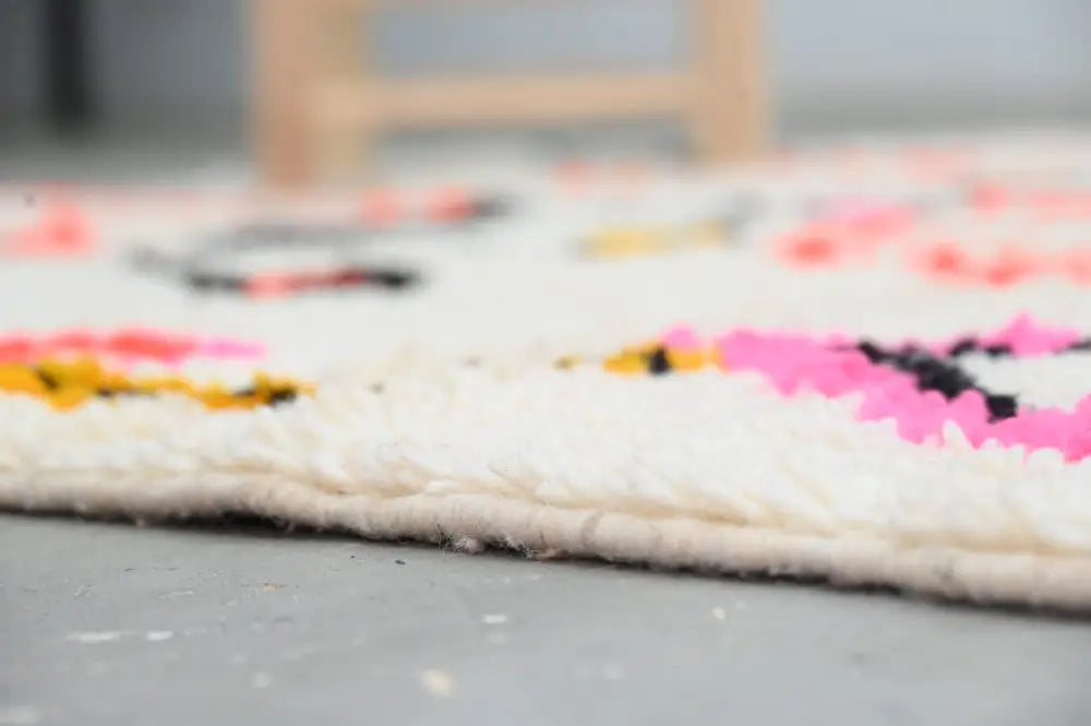 A handmade moroccan azilal rug with a fluffy white base and vibrant pink yellow and black geometric patterns 245x141cm