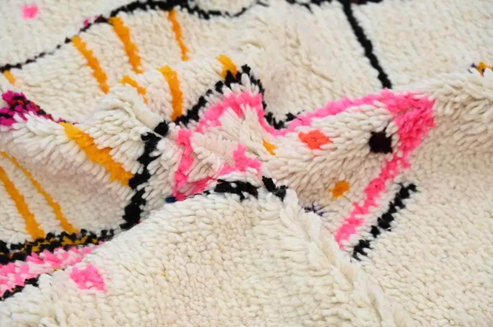 A plush cream-colored moroccan azilal rug with vibrant pink orange and black geometric patterns in thick pile