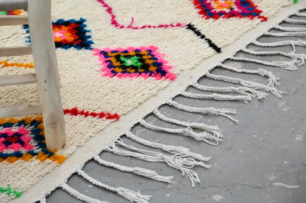 Cream-colored decorbites™ handmade moroccan azilal rug with vibrant geometric patterns and long white fringe 246x142cm