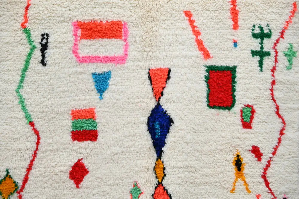 A vibrant fluffy white DecorBites handmade Moroccan Azilal rug with bold red pink blue green and orange geometric patterns