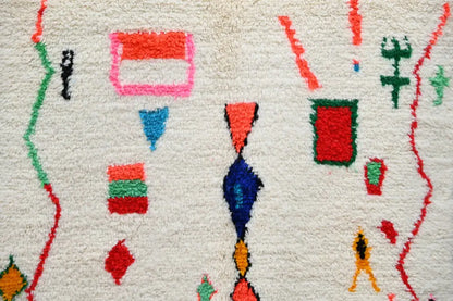A vibrant fluffy white DecorBites handmade Moroccan Azilal rug with bold red pink blue green and orange geometric patterns