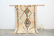 Beige moroccan azilal rug with black orange green and red geometric patterns and fringed edges by decorbites