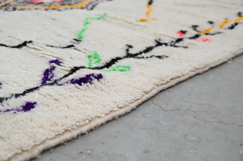 Cream-colored DecorBites™ handmade moroccan azilal rug with intricate black purple green and orange embroidered patterns