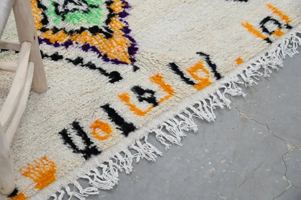 Cream-colored moroccan azilal rug with vibrant orange green and purple geometric patterns and fringed edge 248x151 cm