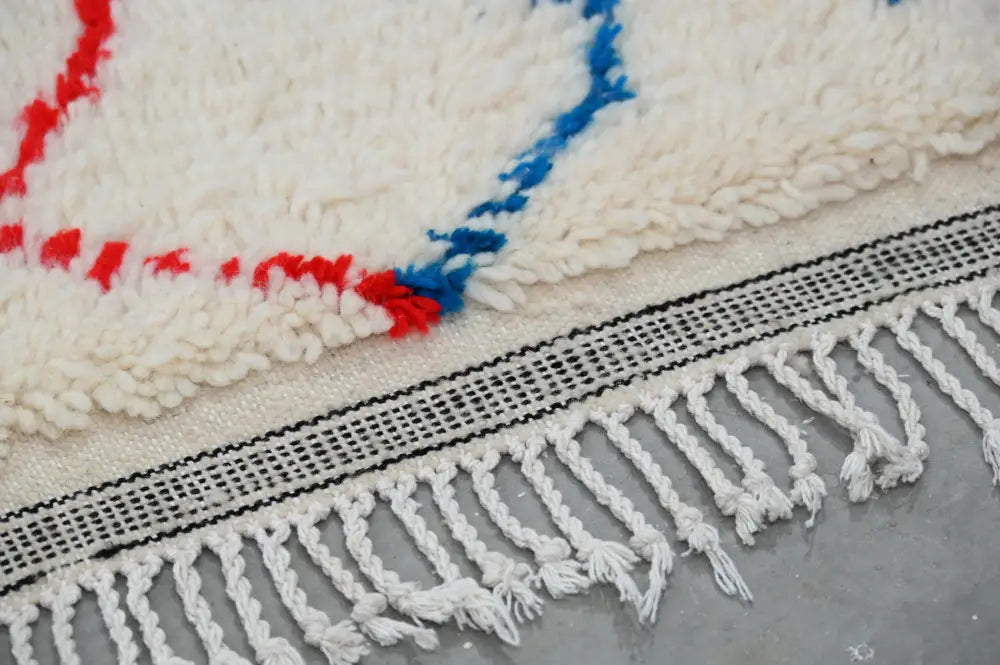 Cream-colored wool moroccan azilal rug with bold red and blue geometric patterns and white fringe 250x154cm